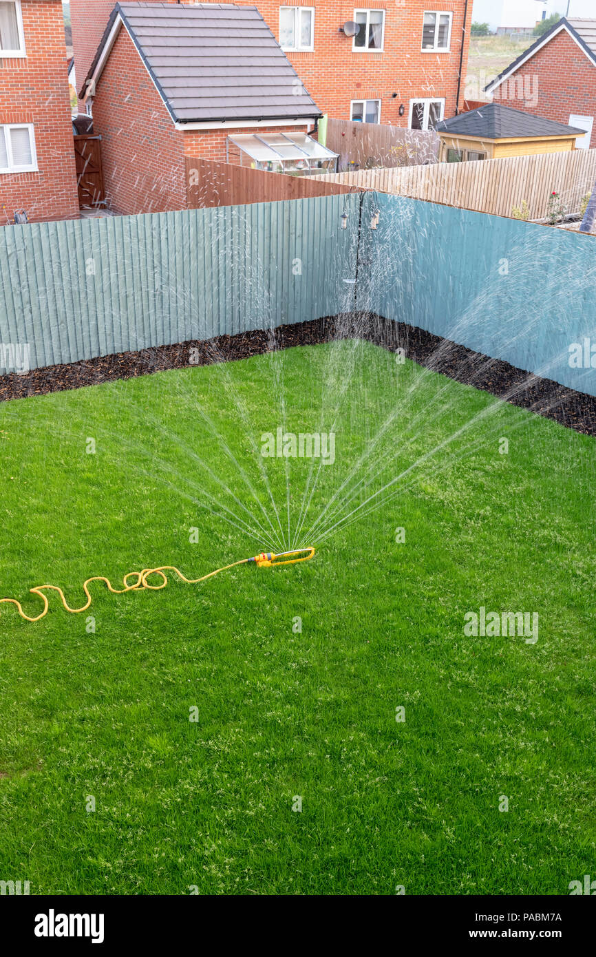 Sprinkler mit einem gelben Schlauch verwendet wird, einen neu verlegten Rasen auf einer Entwicklung des neuen Gehäuses zu Wasser. Stockfoto