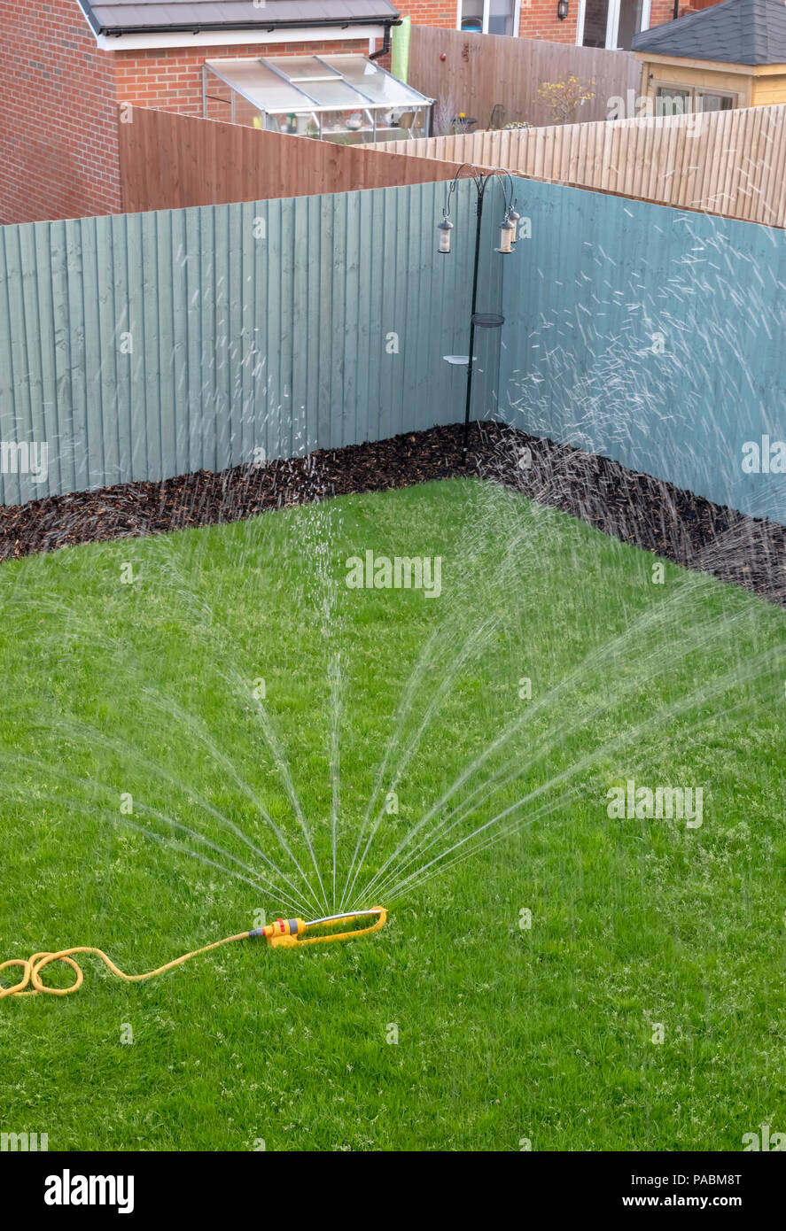 Sprinkler mit einem gelben Schlauch verwendet wird, einen neu verlegten Rasen auf einer Entwicklung des neuen Gehäuses zu Wasser. Stockfoto