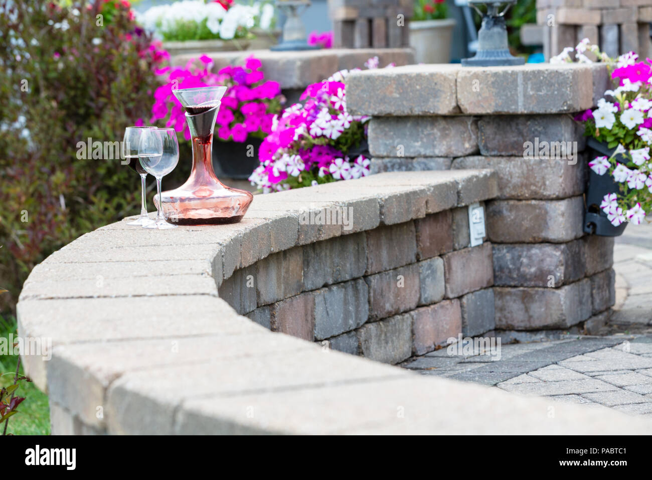 Dekanter Rotwein mit Kohlensäure auf einer gekrümmten Ziegelstein-patio  Wand mit zwei weingläser vor bunten Kübelpflanzen Sommerblumen mit Kopie  Raum Stockfotografie - Alamy