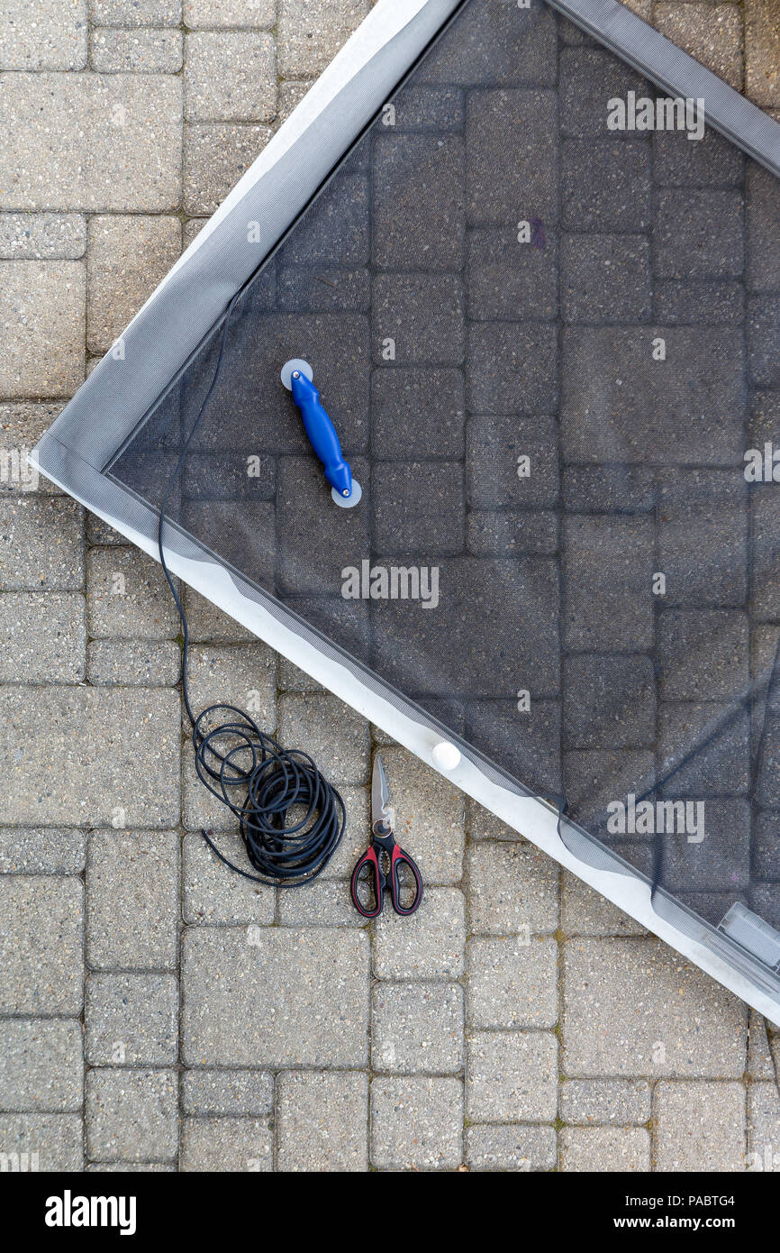 Austausch beschädigter Drahtgeflecht auf einer Terrasse Bildschirm Tür in einer Ansicht von oben der teilweise fertigen Metallrahmen, Pressen und Scheren auf einem Stein Terrasse Stockfoto