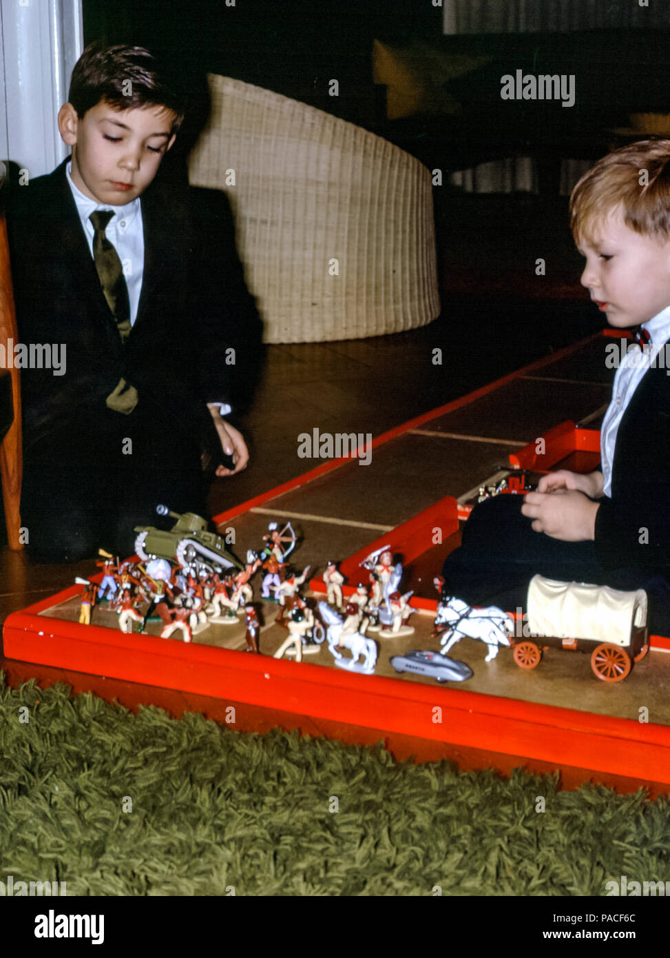 Zwei Jungen, Brüder, trugen Sonntagskleidung mit Anzügen und Krawatten und spielten Cowboys und Indianer in einem Familiensitzraum in den 1960er Jahren Stockfoto