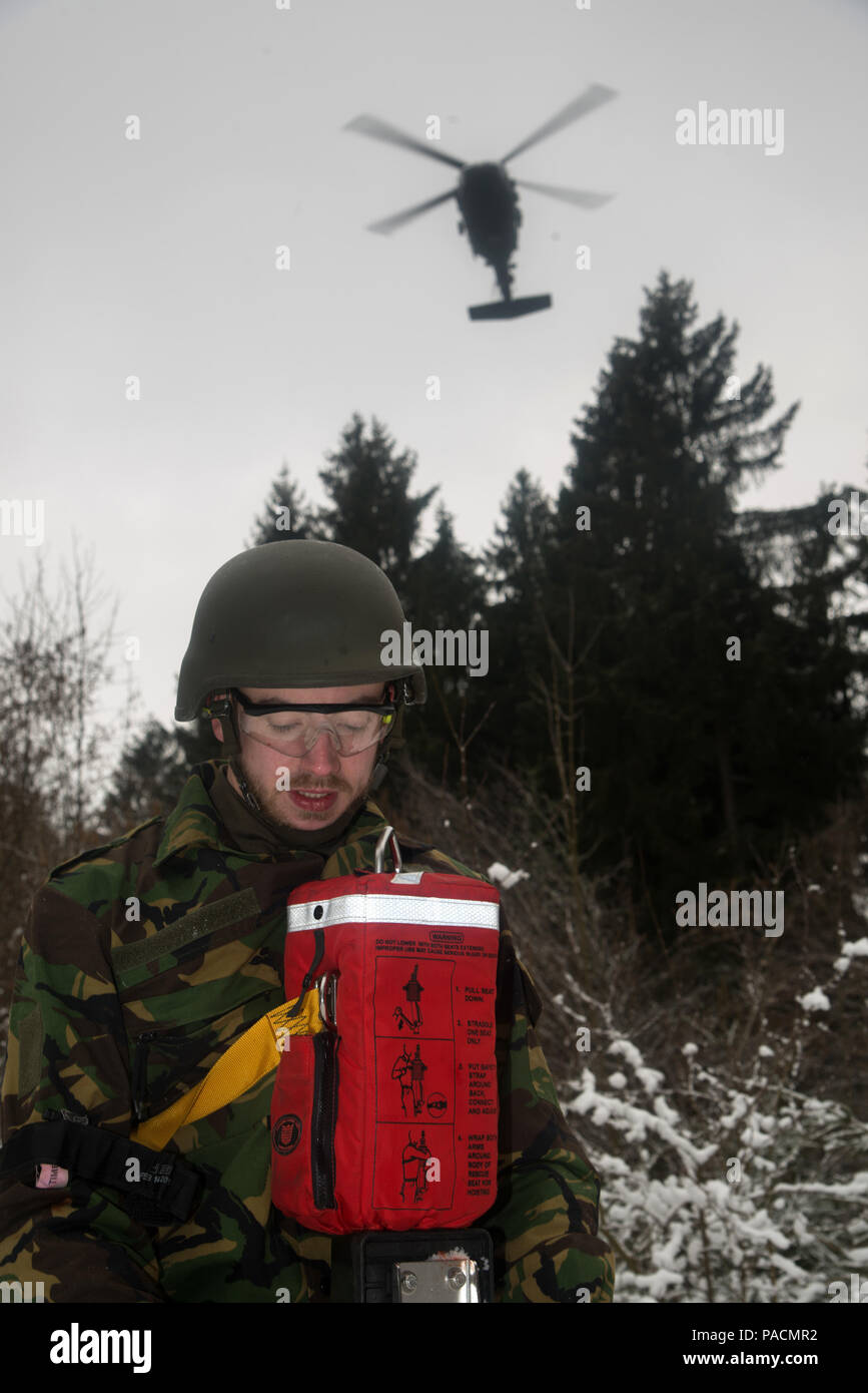 Ein deutscher Soldat, Role player, mit simulierten Schusswunden sitzt auf einem Dschungel penetrator Warten auf dem Black Hawk Hubschrauber ihn weg vom Schlachtfeld bei Tactical Combat Casualty Care Kurs an der Hebevorrichtung, die multinationale Soldaten aus NATO-Ländern die Teilnahme an der internationalen Special Training Center Train the Trainer Kurs, in dem die Hälfte der Teilnehmer Tactical combat Casualty care Lernen und die andere Hälfte Lernen, die Bekämpfung der Unfall- Kurs zu unterrichten. Das Training wurde von General Staufer Kaserne, 16. März 2016 durchgeführt. (U.S. Armee Foto von visuellen Informationen Spezialist Martin Greeso Stockfoto