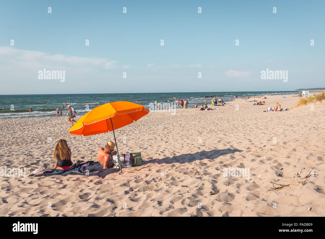 Der Mann und die Frau sitzt auf einer Decke unter einem orange Sonnenschirm am Strand am Nachmittag Sonnenschein, Rorvig, Dänemark, 16. Juli 2018 Stockfoto