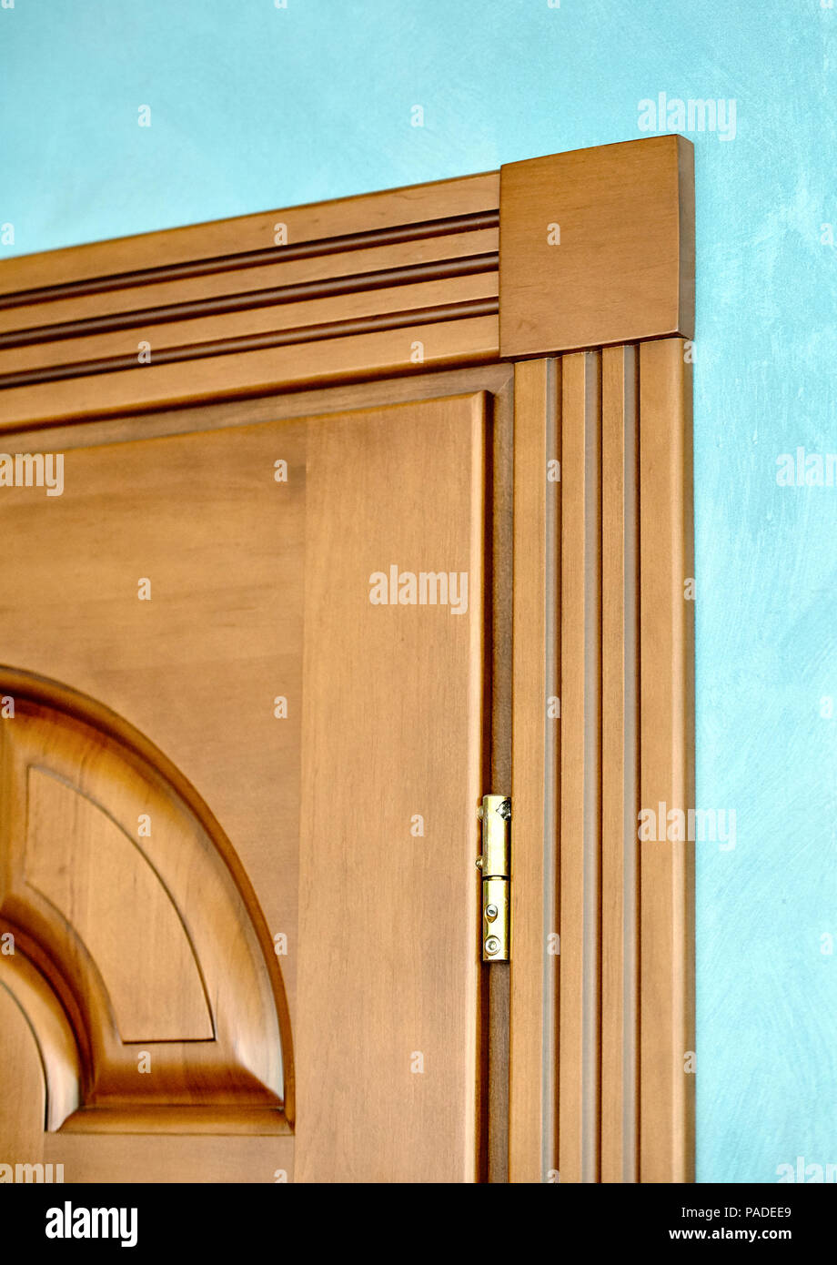 Element der Holztür im Rahmen des braunen Holz geschnitzt geometrischen Ornamenten, klassischen Stil mit vergoldeten Scharniere auf Blau verputzte Wand Hintergrund Nahaufnahme Stockfoto