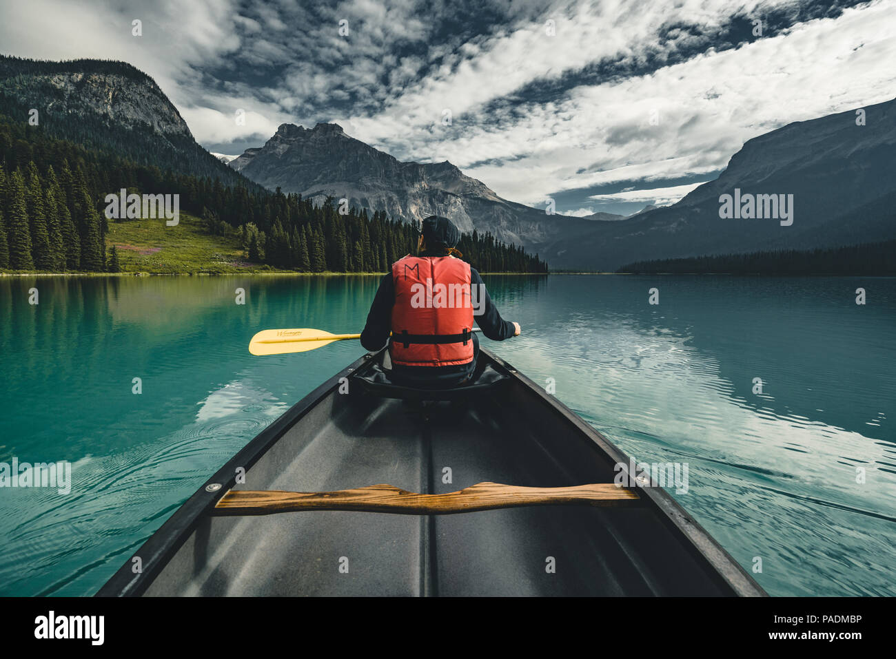 Junger Mann Kanufahren auf dem Emerald Lake in den Rocky Mountains, Kanada mit Kanu und Schwimmweste mit Bergen im Hintergrund blaue Wasser. Stockfoto