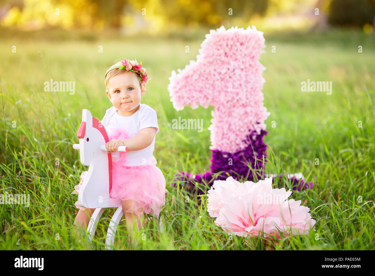 Wunderschöne kleine Mädchen in rosa Kleid reiten auf Holzspielzeug Pferd im Freien. Feier der Ersten Geburtstag Konzept Stockfoto