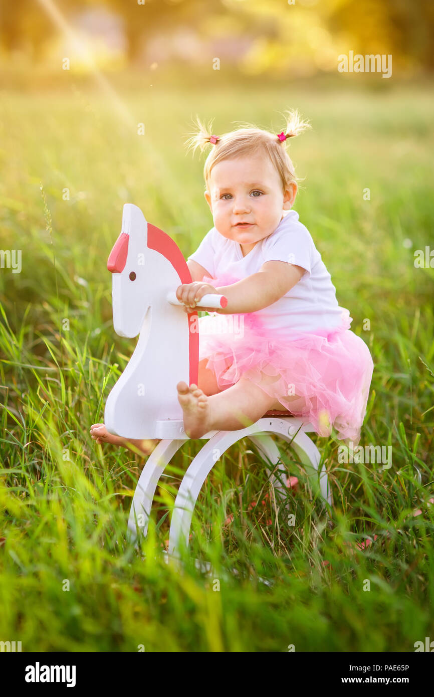 Wunderschöne kleine Mädchen in rosa Kleid reiten auf Holzspielzeug Pferd im Freien Stockfoto