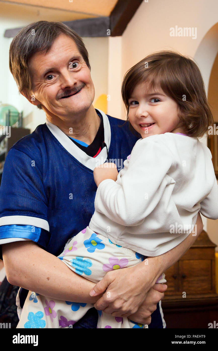Ein Mann mit Down-syndrom seine große Nichte trägt. Sie sind beide glücklich und Blick in die Kamera. Sie trägt Schlafanzug und er hat mindestens drei Stockfoto