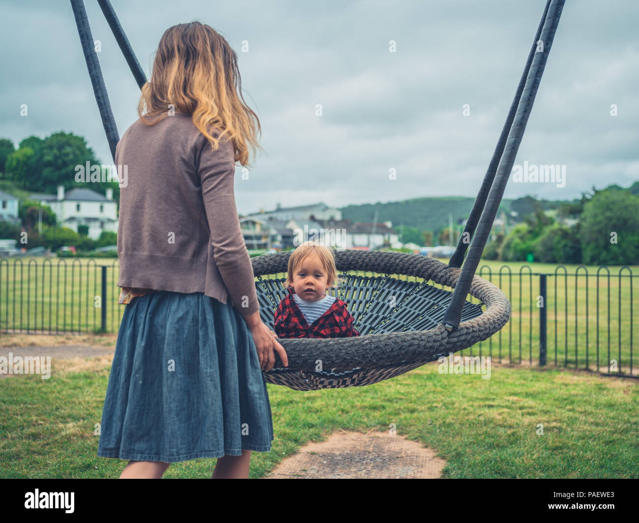 Eine junge Mutter drückt ihr Kind auf einer Schaukel auf dem Spielplatz Stockfoto