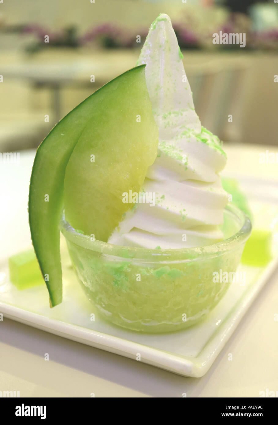 Milch Softeis mit in Scheiben geschnittenen Zuckermelone Obst gekrönt auf Granita in eine Glasschüssel, serviert auf weißen Tisch Stockfoto