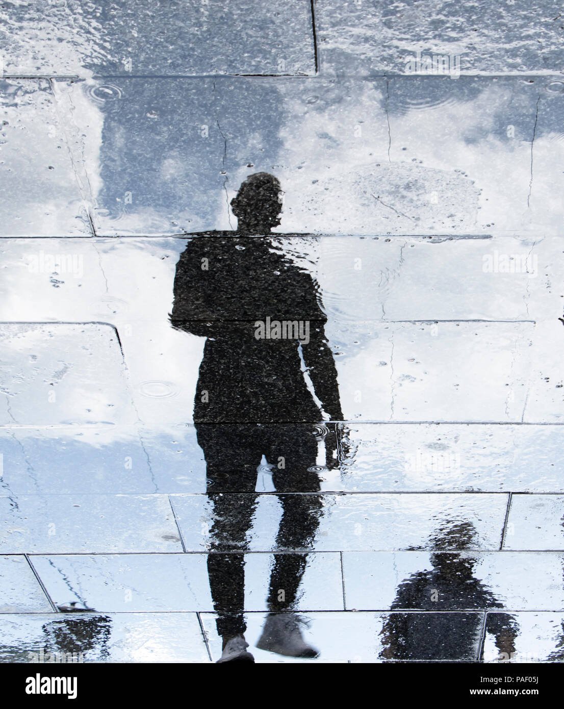Unscharfe Reflexion Schatten Silhouetten von einem jungen Mann an einem regnerischen gemusterten Stadt Bürgersteig Stockfoto