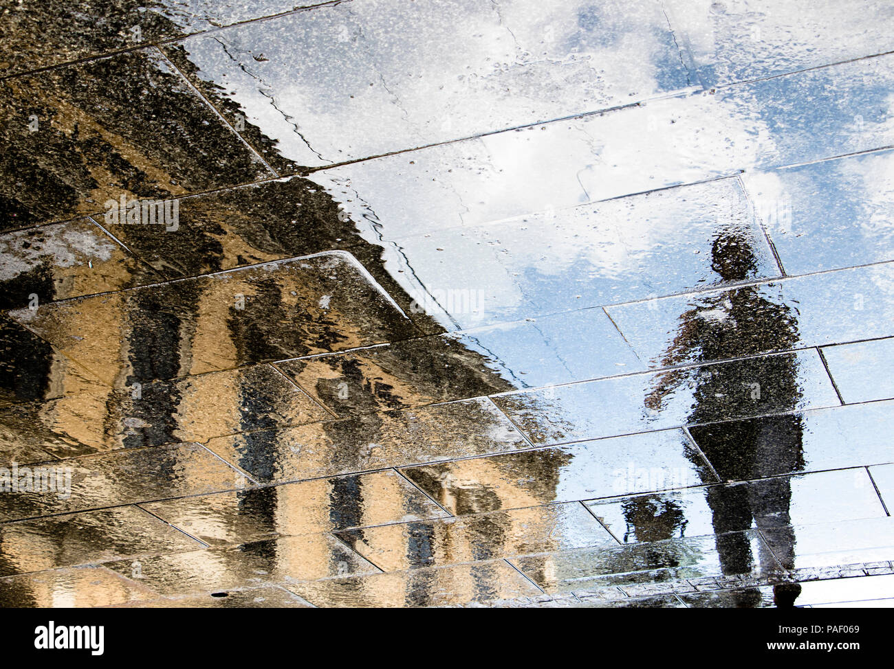 Unscharfe Reflexion Schatten Silhouetten von einer Person zu Fuß an einem regnerischen gemusterten Stadt bürgersteig an einem sonnigen Frühlingstag Stockfoto