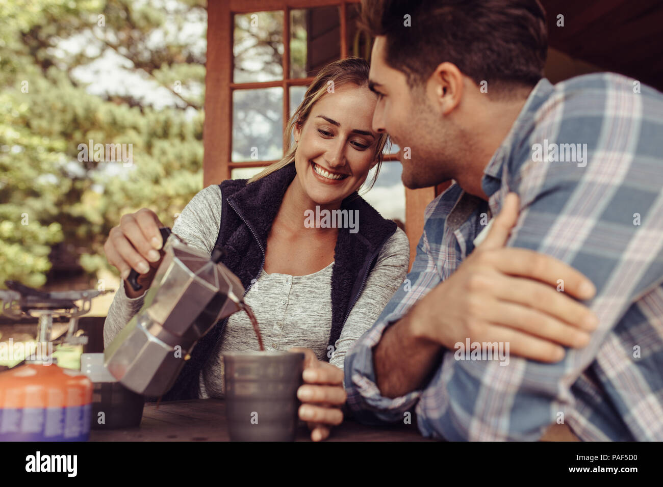 Glückliche junge Frau Kaffee zu ihrem Freund. Paar Kaffee am Frau gießen Kaffee in die