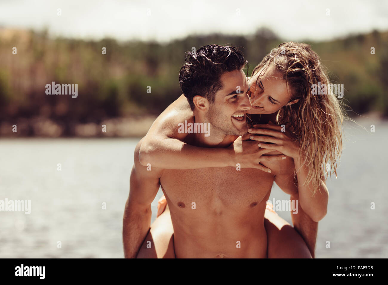 Portrait der romantischen jungen Mann huckepack seine Freundin. Junges Paar, das Spaß am Seeufer. Stockfoto