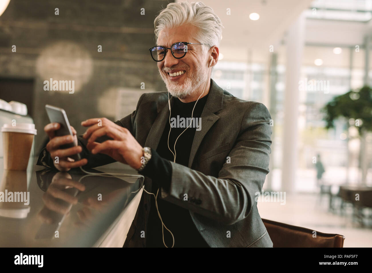 Reifen texting Geschäftsmann Nachricht auf Smart Phone beim Hören von Musik über Kopfhörer und genießen im Coffee Shop. Mitte der erwachsenen Mann in Anzug bei entspannenden Stockfoto