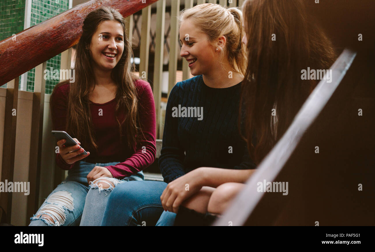 Junge Frauen sitzen auf der Treppe der Universität während der Pause. Drei High School Mädchen sitzen auf der Treppe im Freien mit Handy. Stockfoto