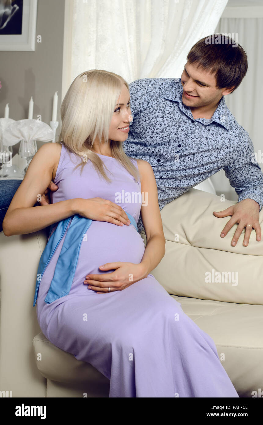 Junge schwangere Frau mit Mann auf einem weißen Sofa im Licht Home Zimmer Stockfoto