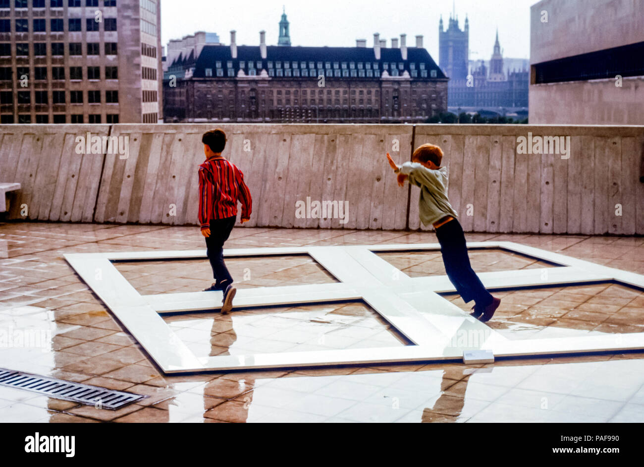 Junge Jungs haben Spaß beim Springen über moderne Kunstwerke auf dem Außendeck der Hayward Gallery, South Bank, London, England, Großbritannien in den 1960er Jahren. Der kleine Junge ist dabei, zu stolpern und auf den Rand der Kunstinstallation zu fallen Stockfoto