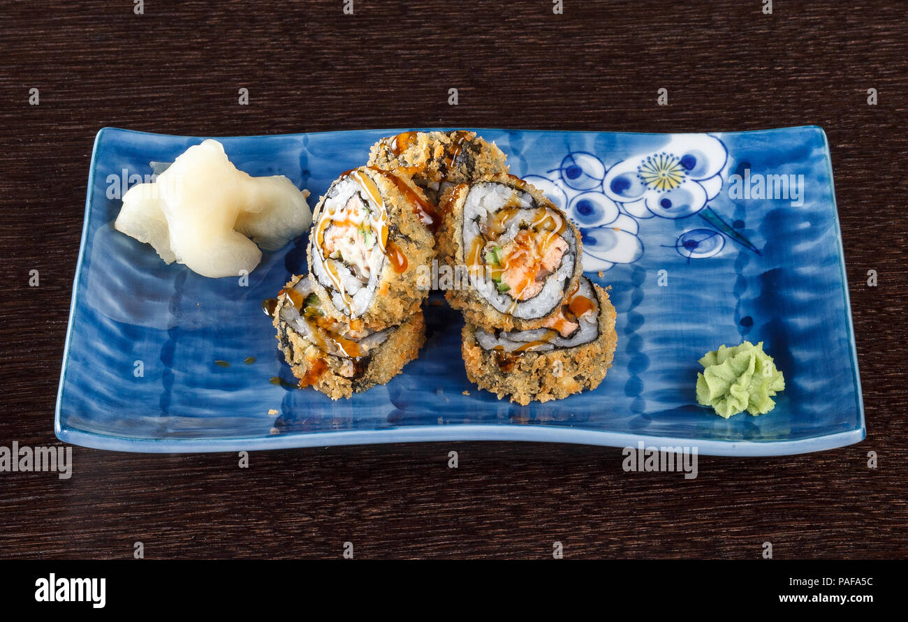 Heißes gebratenes Sushi rollen auf einem Teller mit Lachs und Gurke auf Holztisch. Stockfoto