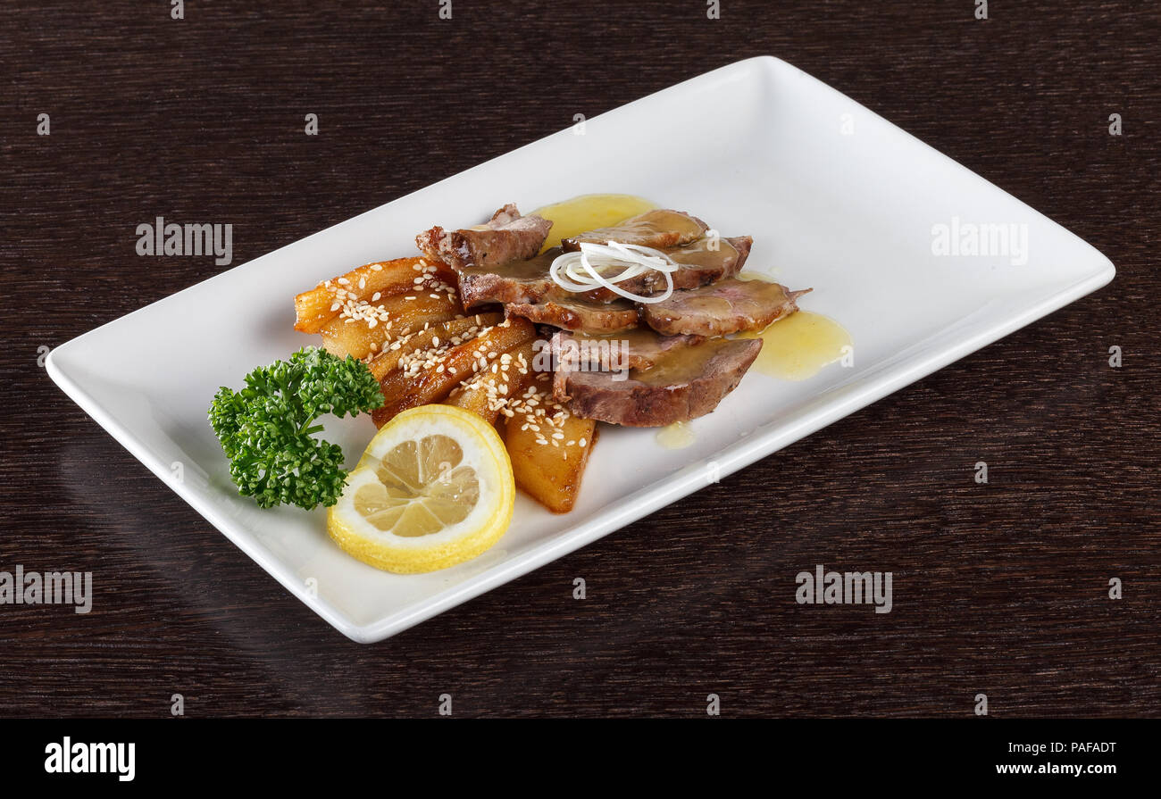 Brocken Fleisch mit Sauce, Bratkartoffeln und einer Scheibe Zitrone und Petersilie auf weiße Platte. Europäische Küche. Seitenansicht Stockfoto