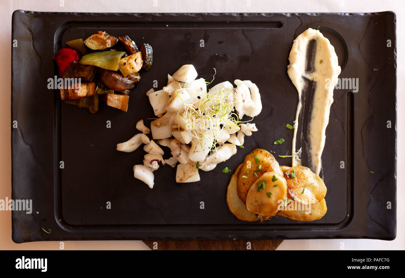 Kalmare Rezept mit Kartoffeln, Gemüse und Soße auf einer schwarzen Schiefer  Stockfotografie - Alamy