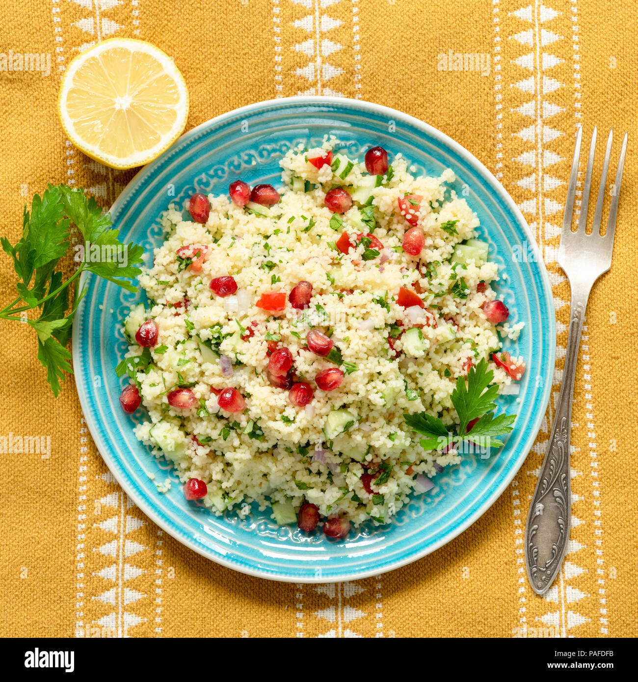 Taboulé Couscous Salat mit Granatapfel auf Blau Blaugrün Platte über ethnische Textil. Ansicht von oben, Quadrat Erntegut Stockfoto