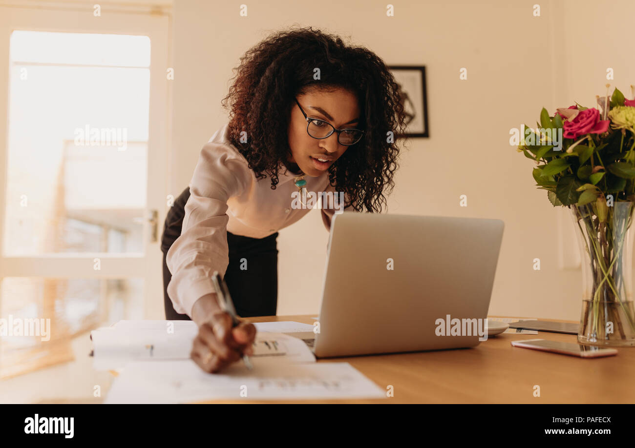 Geschäftsfrau Notizen auf einem Laptop zu Hause suchen. Unternehmerin lehnte sich über den Tisch Notizen zu schreiben, während am Notebook suchen. Stockfoto