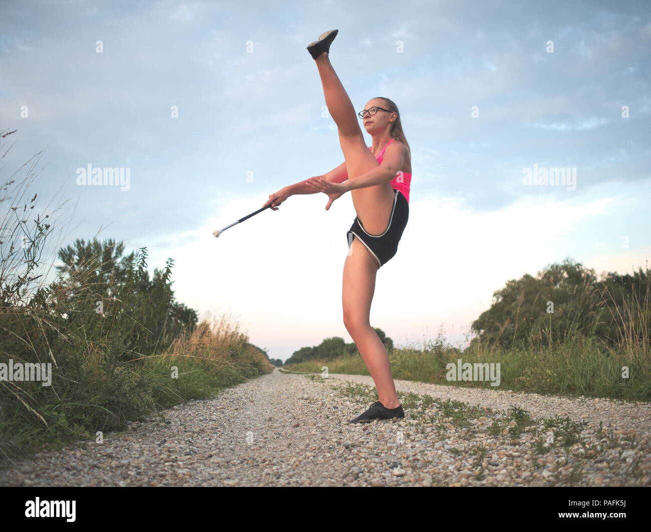 Bebrillter blonder Teen Majorette Mädchen Twirling Baton im Freien Training Kleidung Stockfoto