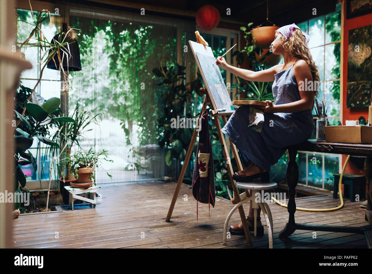 Innen- schuss der professionellen Künstlerin Gemälde auf Leinwand im Studio mit Pflanzen. Stockfoto