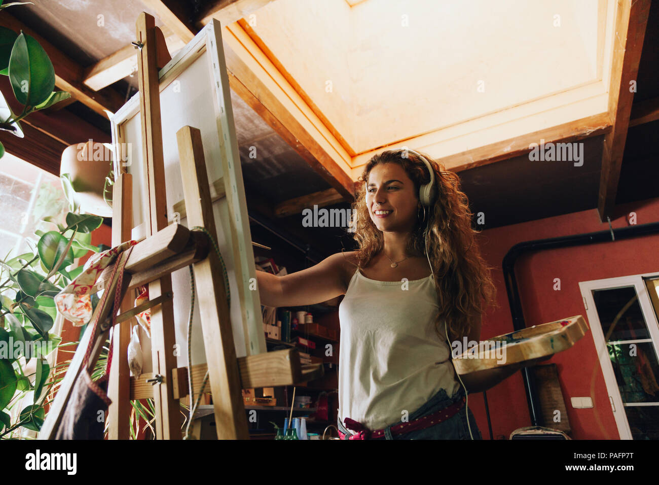 Innen- schuss von professionellen lächelnd weibliche Künstler mit Kopfhörern Gemälde auf Leinwand im Studio. Stockfoto