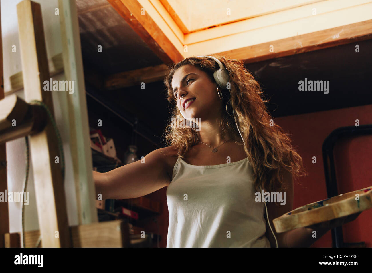 Innen- schuss von professionellen lächelnd weibliche Künstler mit Kopfhörern Gemälde auf Leinwand im Studio. Stockfoto