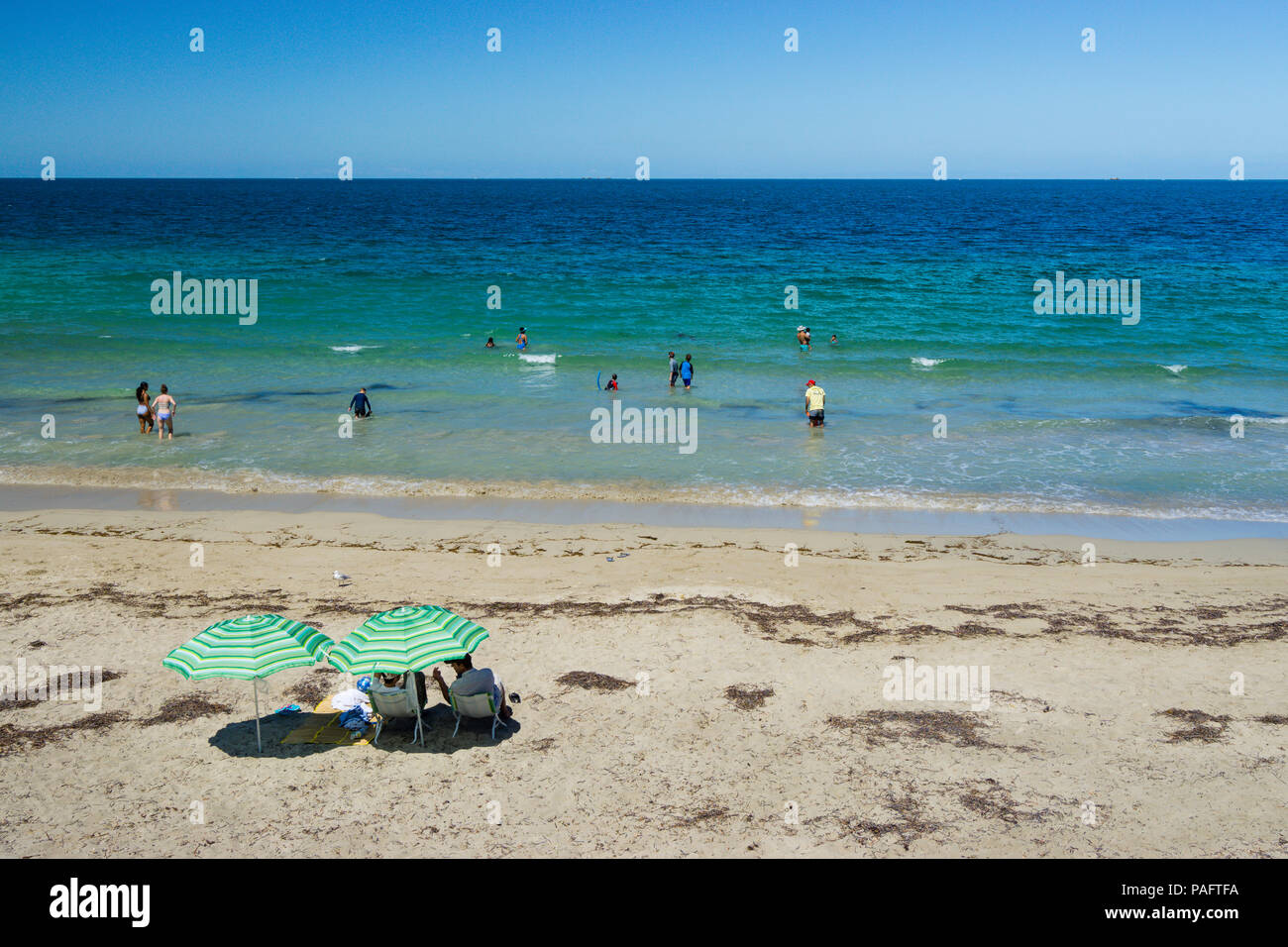 Menschen sitzen unter dem Dach am weißen Sandstrand beobachten Schwimmer. Shoalwater Bay Rockingham Western Australia Stockfoto