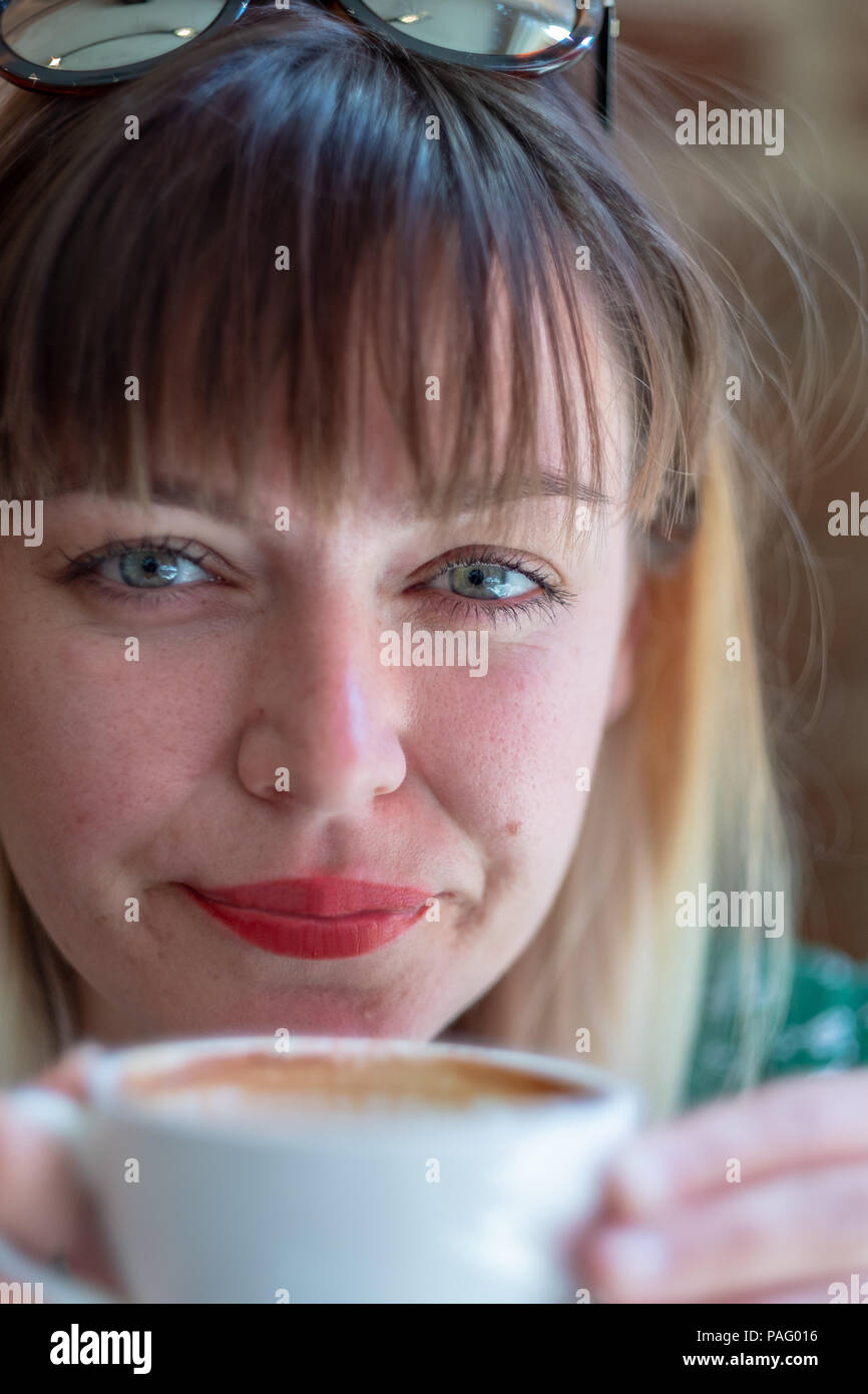 Eine junge Frau trinkt einen Kaffee in einem Café in die Kamera schaut Stockfoto