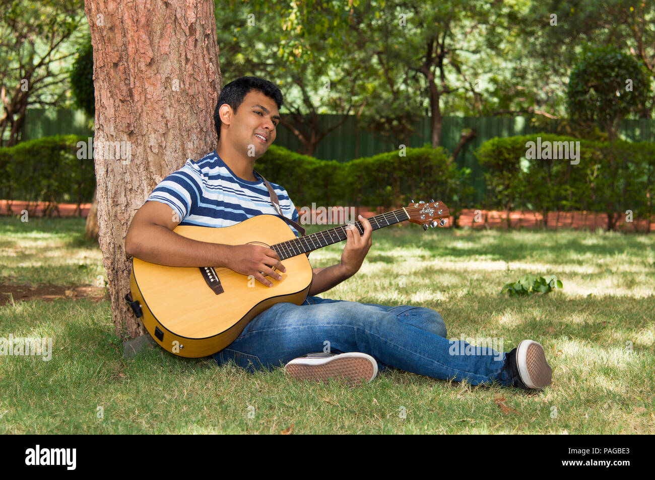 Junger Mann mit Gitarre unter Baum Stockfoto