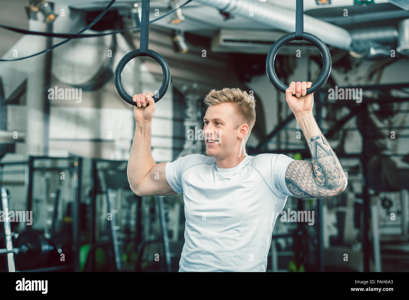 Hübscher junger Mann mit starken Armen hängend an Gymnastik Ringe Stockfoto
