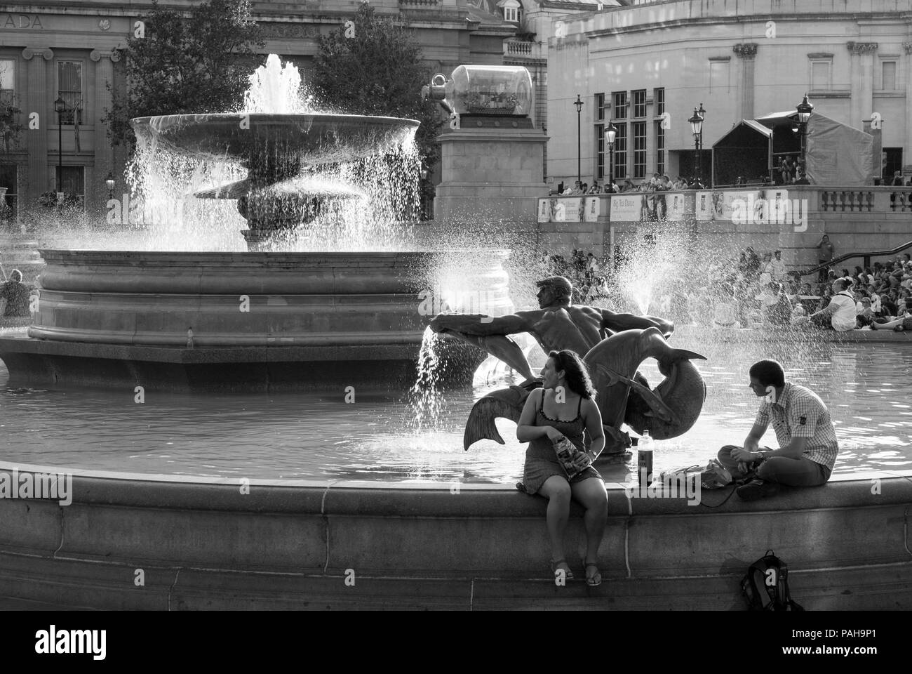 Ein schwarz-weißes Bild von einem Mann und einer Frau, die ein Mittagessen genießen und am Rande des Brunnens am Trafalgar Square in London sitzen Stockfoto