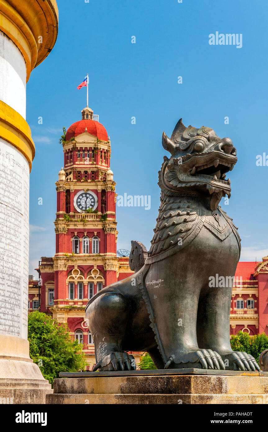 Ein halb Löwe und halb Drache Stein Skulptur am Fuße des Independence Monument mit High Court Gebäude hinter, Yangon, Myanmar Stockfoto