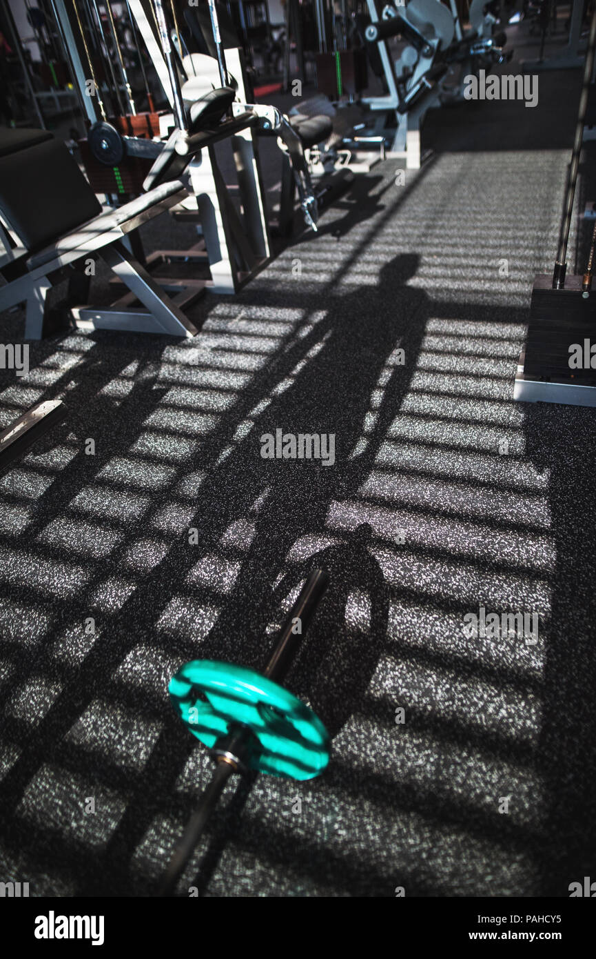 Fitnessraum mit verschiedenen Trainingsgeräten, der Schatten einer Person heraus zu arbeiten. Stockfoto