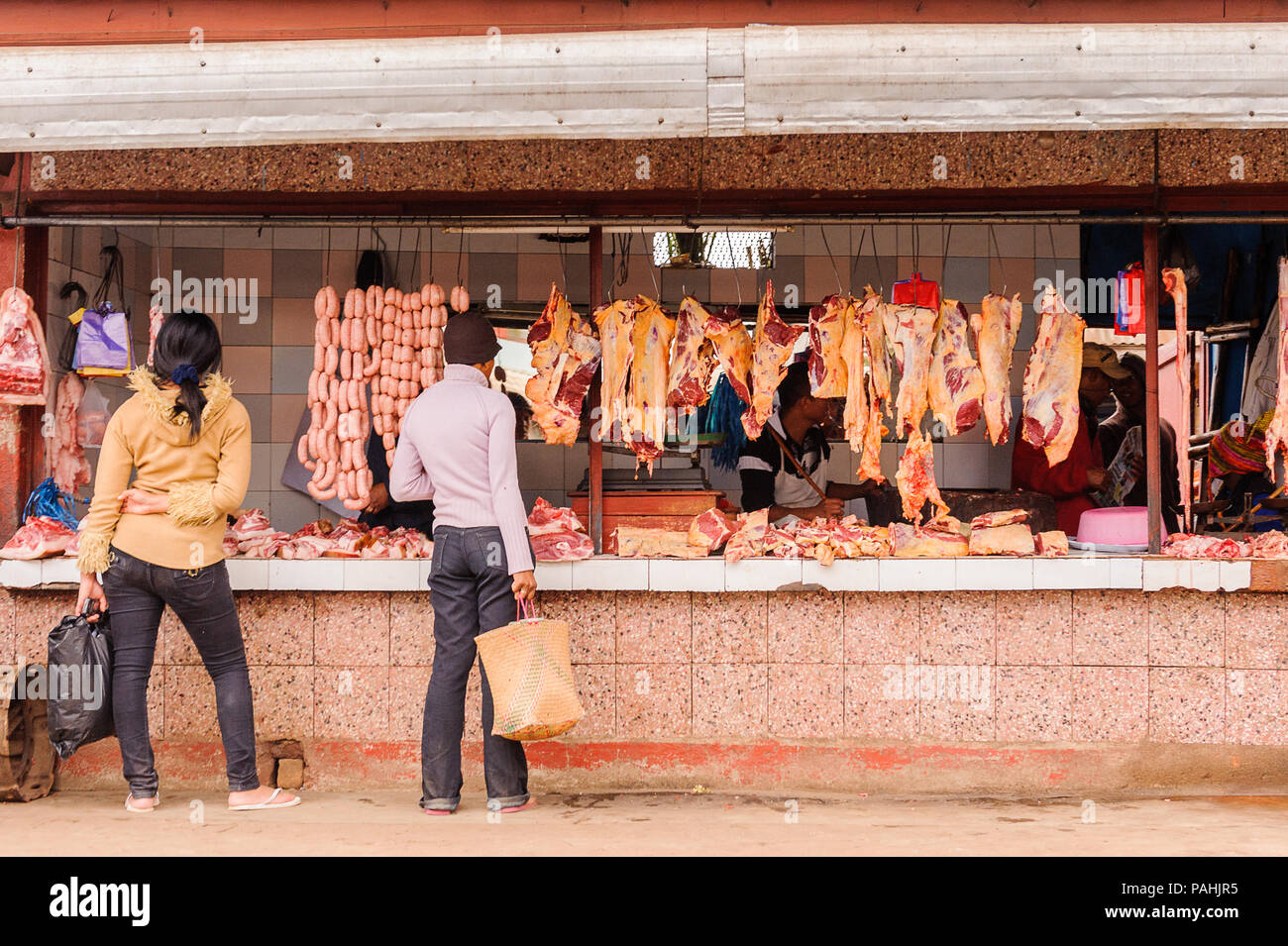 ANTANANARIVO, Madagaskar - 29. JUNI 2011: Unbekannter Madagaskar Mann wählt Fleisch- und Wurstwaren auf dem Markt. Die Menschen leiden an Armut in Madagaskar Stockfoto