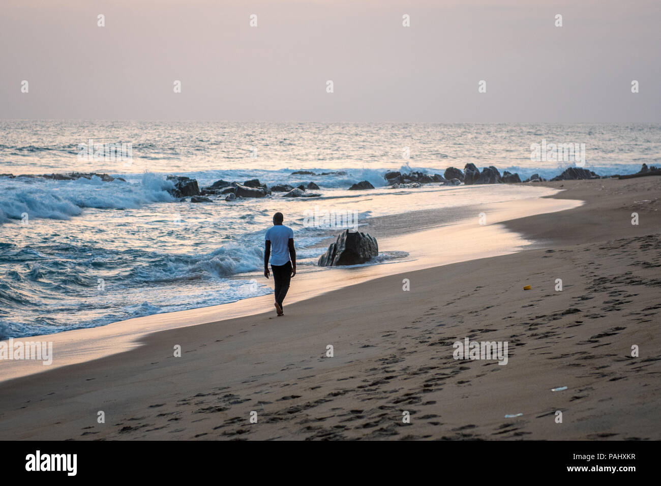 Ein Mann Spaziergänge am Wasser entlang in der Abenddämmerung am Strand in Monrovia, Liberia Stockfoto