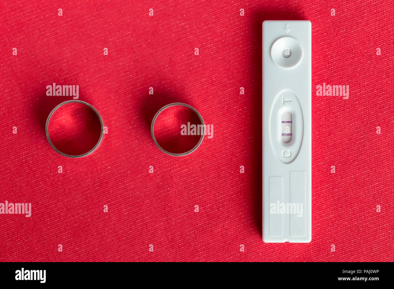 Zwei Eheringe und einen positiven Schwangerschaftstest. Konzeptionelle Ankündigung der Ankunft eines Kindes. Stockfoto