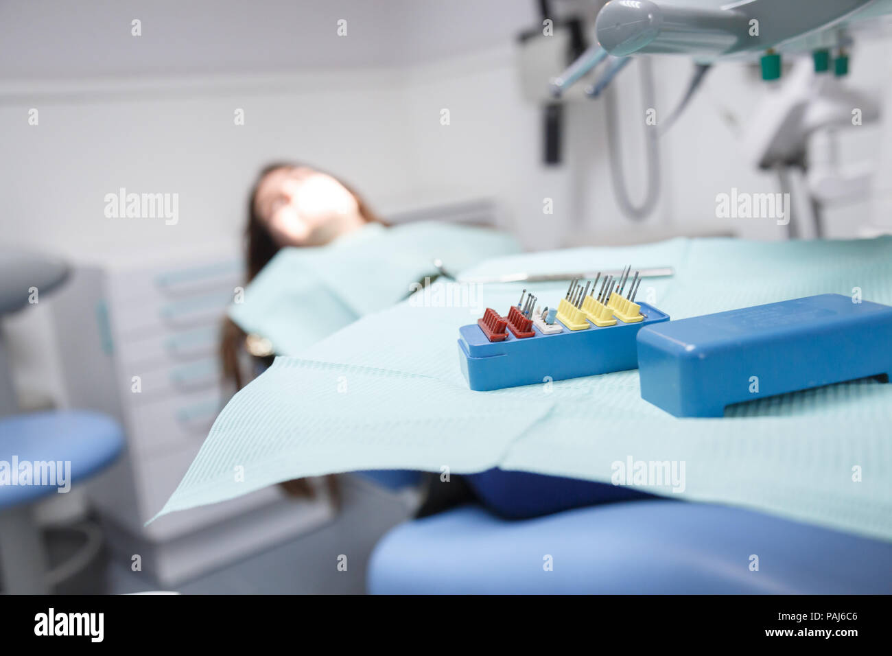 Junge weibliche im Behandlungsstuhl sitzen in Klinik Zimmer in Soft Focus mit Ausrüstung und Instrumente für die Reinigung des Mund und zum Entfernen von Kavitäten Stockfoto
