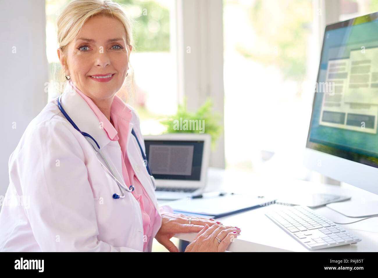 Lächelnd älteren weiblichen Forschung Arzt mit Computer und Laptop, während am Schreibtisch arbeiten. Stockfoto