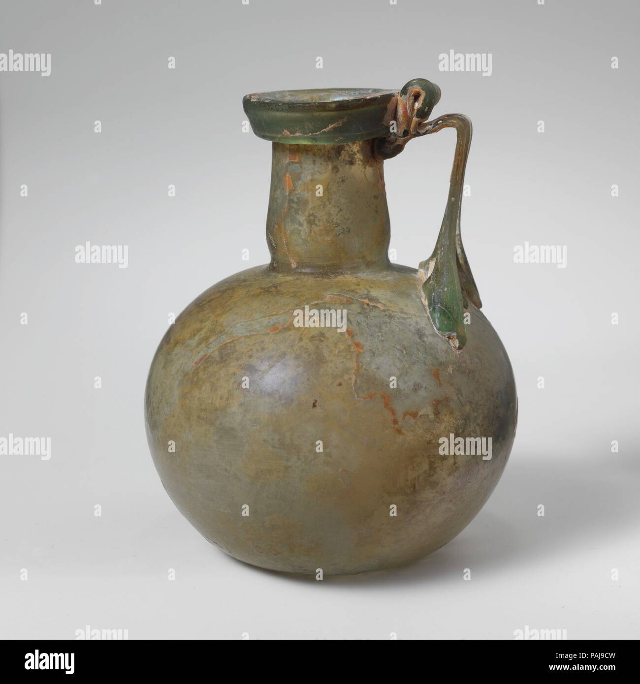 Glaskanne. Kultur: Roman. Abmessungen: 4 5/16 in. (10,9 cm) Andere: 3 5/16 in. (8,4 cm) Durchm. Von rim: 1 1/2 in. (3,9 cm). Datum: Mitte 1.-2. Jh. N.CHR.. Transluzent blau grün; in gleicher Farbe. Kragen rim ausgeklappt, nach unten und oben, mit abgerundetem äußeren vertikalen Lippe; leicht trichterförmig zylindrische Hals, mit schnittspuren an der Basis; kugelförmigen Körper; konkave Unterseite; Strap Griff in vier Kralle Pads zu schultern, erstellten und horizontal gedreht, mit einem vertikalen als Daumen oben Rim falten und dann schleppte am äußeren Rand von Rim und oben am Hals. Intakt; wenige Blasen im Körper, aber m Stockfoto