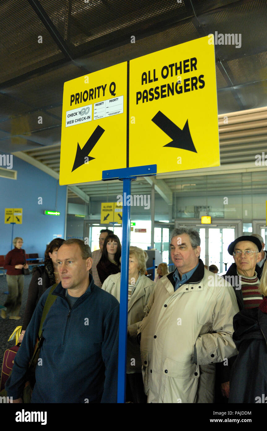 Passagiere in der Warteschlange unter dem Zeichen für "Priority Q'Web Check-in und auf "Alle anderen Passagiere in der Abfahrt - Lounge Stockfoto