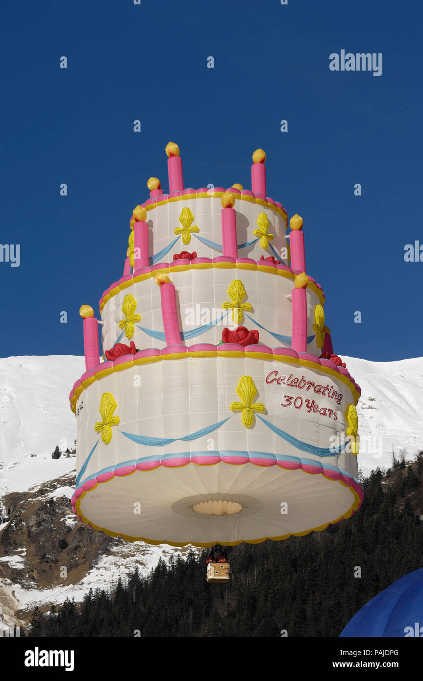 Ein lindstrand Kuchen Special-form Heißluft-ballon Fliegen mit Bäumen, Schnee und Berge hinter Stockfoto