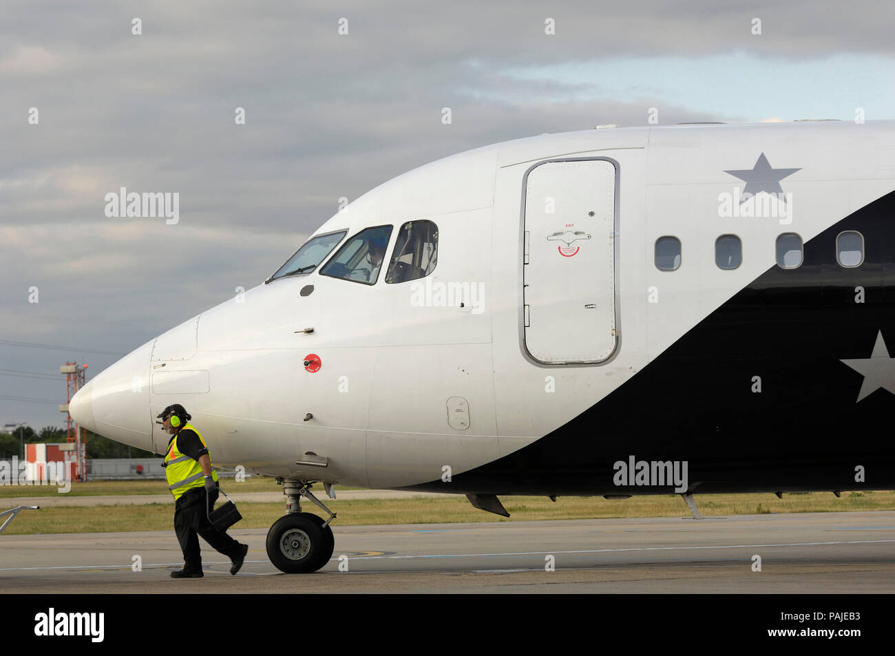 Mann Gelb hohe-viz Waffenrock und Ohr - Verteidiger Keil entfernen aus Bugrad des Titan Airways BAE 146-200 QC am London City geparkt Stockfoto