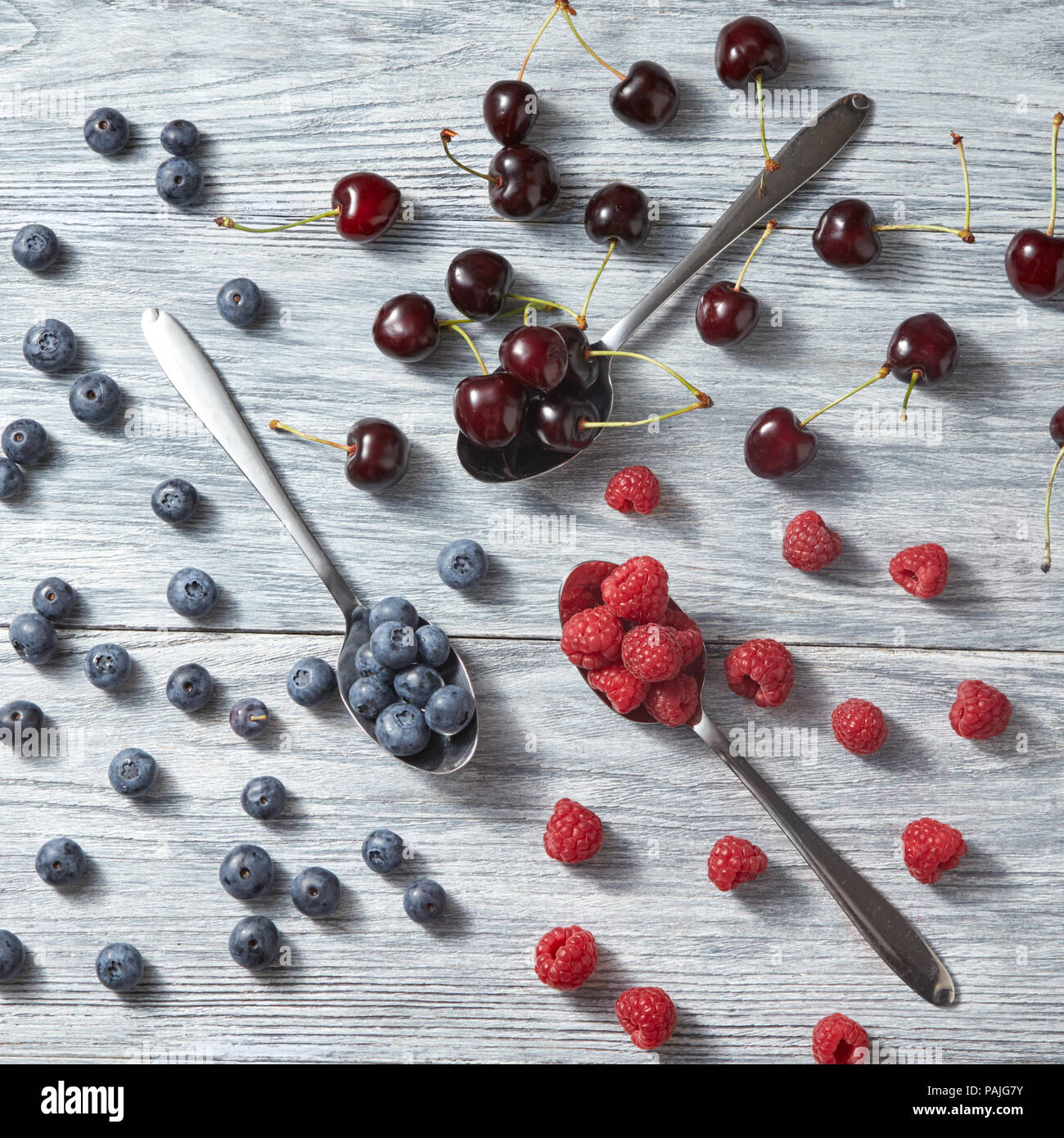 Mischung aus frische organische Beeren Muster von Blaubeeren, Kirschen, Himbeeren auf einem grauen Hintergrund aus Holz. Ansicht von oben. Stockfoto