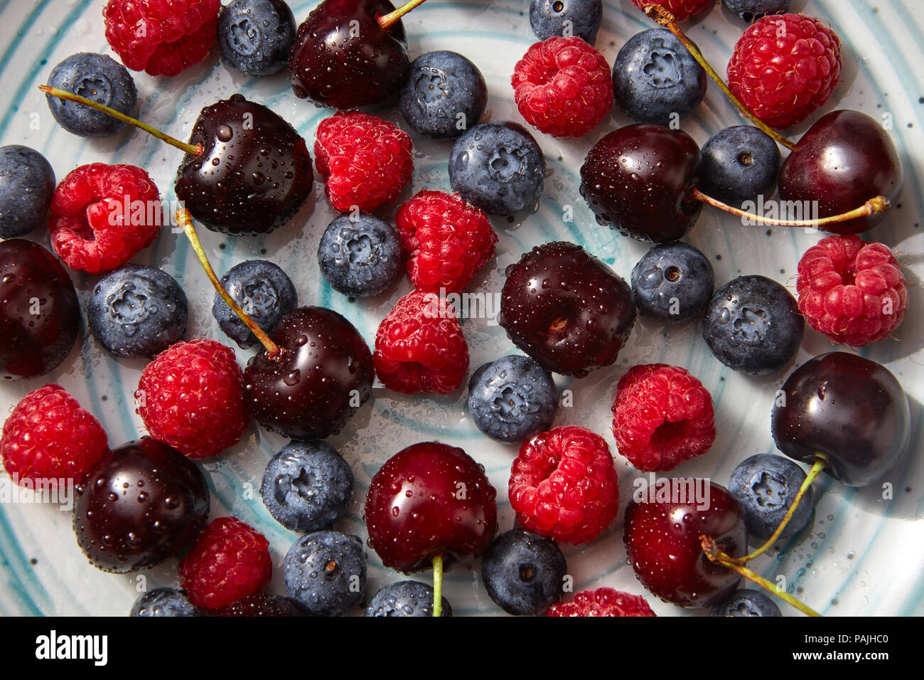 Süße Kirschen, Himbeeren, Blaubeeren mit Tropfen Wasser auf Sie. Natürliche organische Beeren close-up Hintergrund. Stockfoto