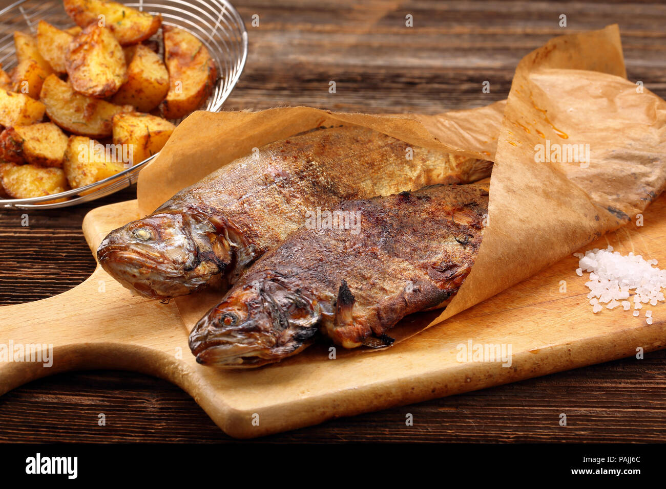 Gegrillter Fisch mit Kartoffeln in Papier eingewickelt auf Holz- Hintergrund Stockfoto